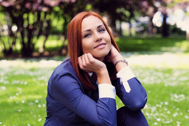 Retrato de mulher ruiva sorridente descansando ao ar livre.