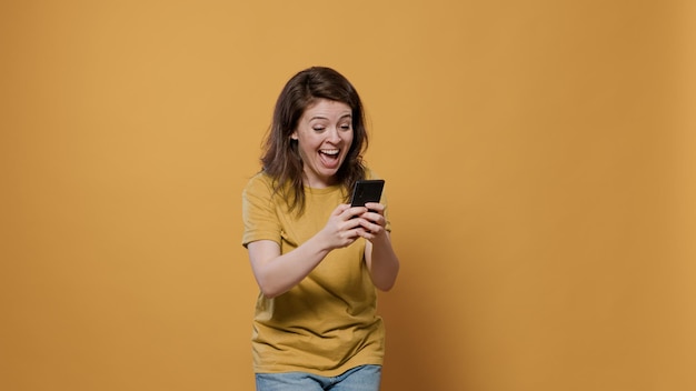 Foto grátis retrato de mulher segurando smartphone olhando para o amigo de mensagens de texto com tela sensível ao toque recebendo boas notícias extraordinárias querendo pular de alegria. pessoa sorridente usando telefone celular sobrecarregada de felicidade.