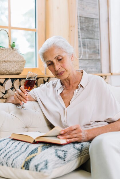 Retrato, de, mulher sênior, copo segurando, de, bebida, livro leitura