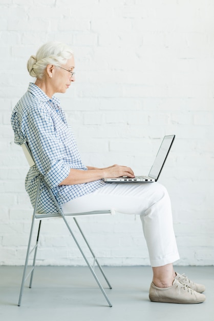 Retrato, de, mulher sênior, sentando, ligado, cadeira, usando computador portátil