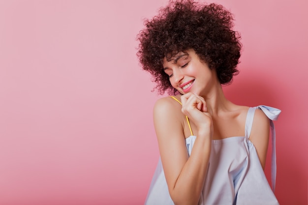 Foto grátis retrato de mulher sensível de cabelos curtos com cachos e blusa azul celeste posa com um sorriso encantador em rosa