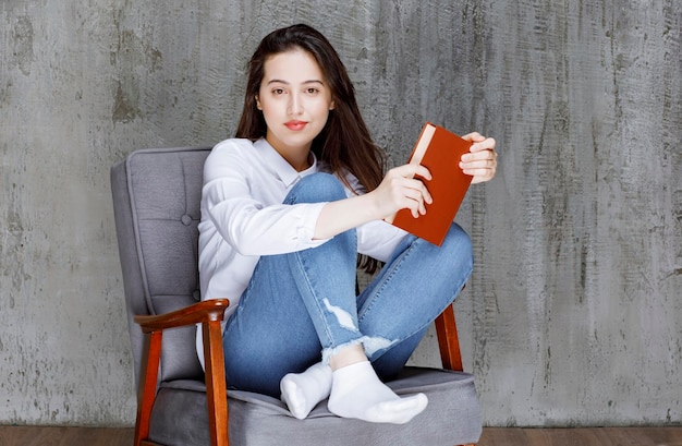 Retrato de mulher sentada na poltrona com livro posando. Foto de alta qualidade