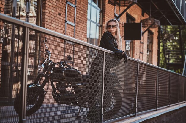 Retrato de mulher sexy madura em pé na varanda ao lado de sua moto.