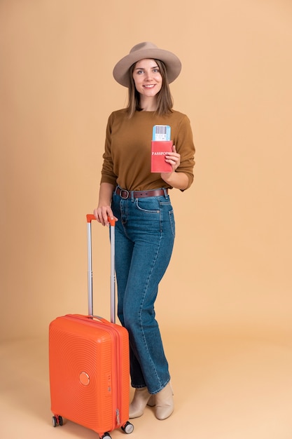 Retrato de mulher sorridente com chapéu segurando passaporte e bagagem