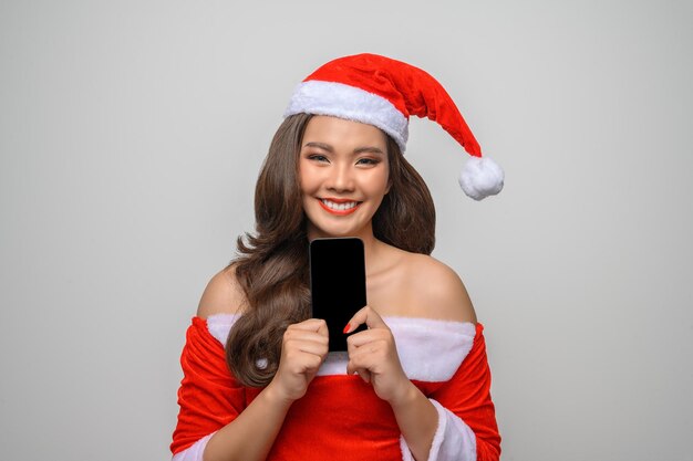 Retrato de mulher sorridente em papai noel vermelho mostrando smartphone