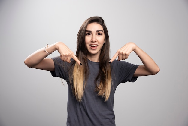 Retrato de mulher sorridente, mostrando sua t-shirt sobre fundo cinza.