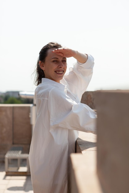 Retrato de mulher turista tendo a mão na cabeça, apreciando a paisagem da cidade metropolitana do edifício ponto de observação do telhado durante as férias de verão. Vista panorâmica de edifícios urbanos