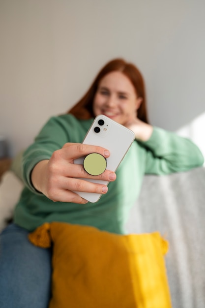Retrato de mulher usando seu smartphone em casa no sofá, segurando na tomada pop