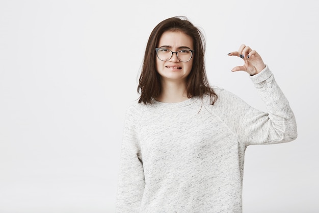 Retrato de mulheres atraentes inteligentes em copos, expressando antipatia e mostrando algo pequeno