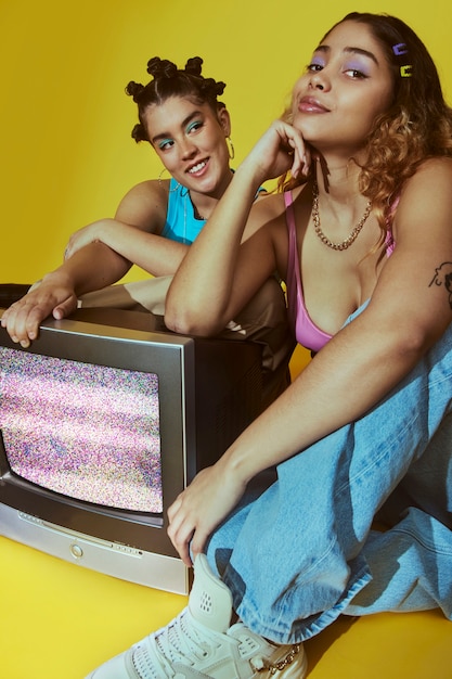 Retrato de mulheres jovens no estilo de moda dos anos 2000 posando com tv