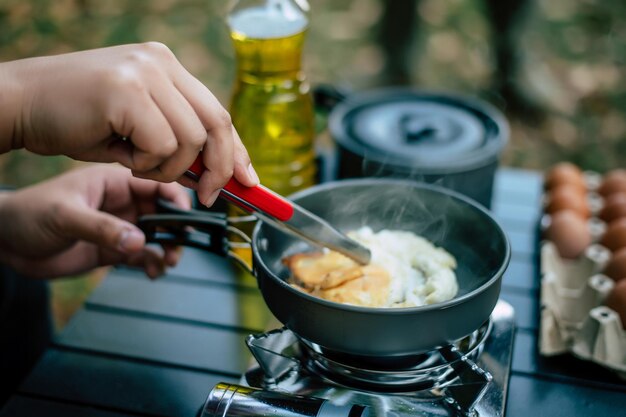 Retrato de óculos de homem viajante asiático fritando um saboroso ovo frito em uma panela quente no acampamento Cozinhar ao ar livre viajando conceito de estilo de vida de acampamento