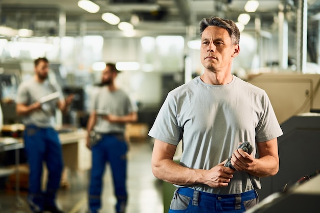 Retrato de operador CNC adulto médio olhando para longe enquanto está em uma fábrica