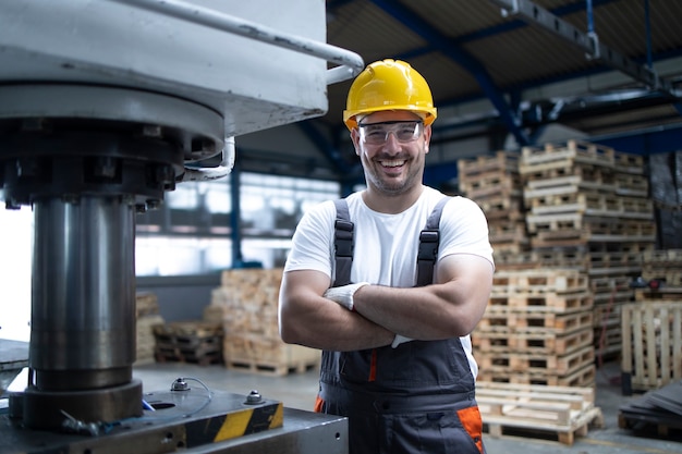 Retrato de operário com os braços cruzados em pé perto da máquina de perfuração em planta industrial