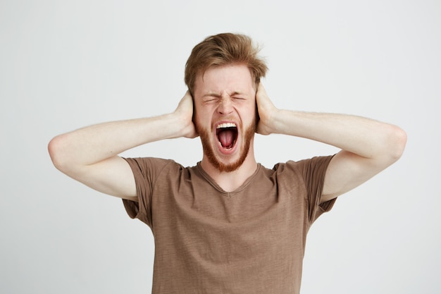 Retrato de orelhas de fechamento do jovem homem irritado emotivo gritando gritando.