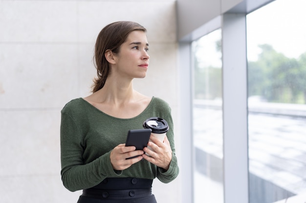 Retrato, de, pensativo, mulher jovem, segurando telefone móvel, e, café