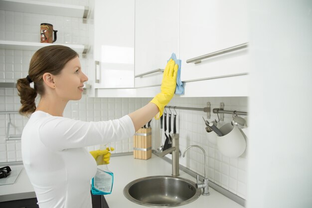 Retrato de perfil de mulher atraente limpando cozinha branca clos