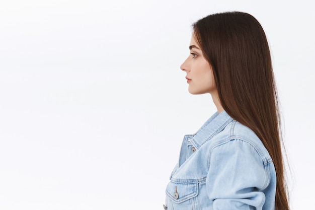 Retrato de perfil sério, determinado e confiante, atraente mulher moderna dos anos 20 em jaqueta jeans, em pé no elevador ou no metrô, esperando na fila com expressão calma e desinteressada