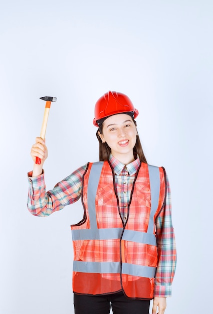 Retrato de reparador feminino em pé uniforme com um martelo sobre uma parede branca.