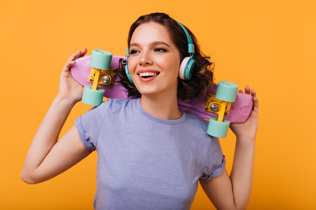 Retrato de rir alegre menina curtindo música. Romântica senhora caucasiana com skate colorido sorrindo.