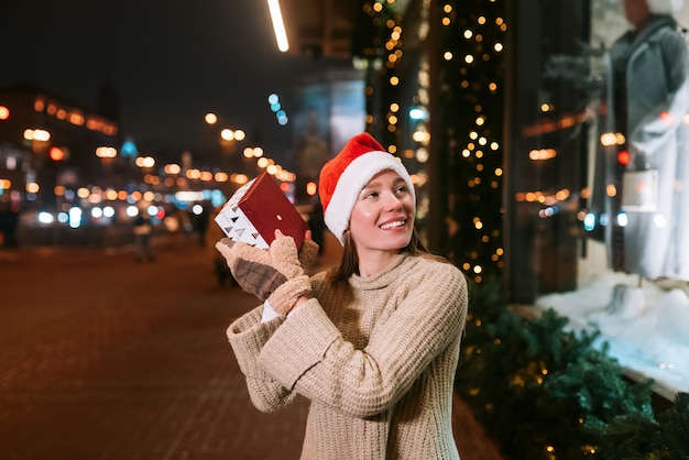 Retrato de rua à noite de uma jovem mulher bonita agindo emocionado. Luzes festivas de guirlanda.