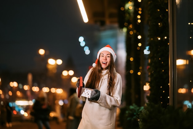 Retrato de rua à noite de uma jovem mulher bonita agindo emocionado. Luzes festivas de guirlanda.