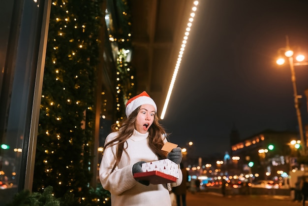 Retrato de rua à noite de uma jovem mulher bonita agindo emocionado. Luzes festivas de guirlanda.