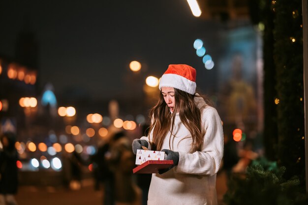 Retrato de rua à noite de uma jovem mulher bonita agindo emocionado. Luzes festivas de guirlanda.