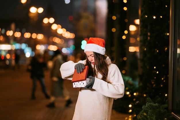 Retrato de rua à noite de uma jovem mulher bonita agindo emocionado. luzes festivas de guirlanda.