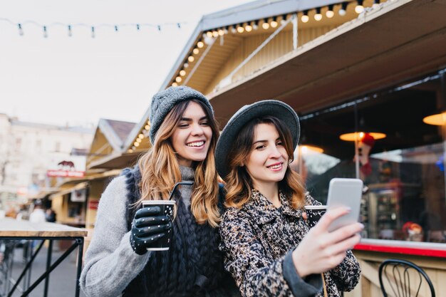 Retrato de selfie de alegres mulheres na moda, se divertindo na rua ensolarada da cidade. Look estiloso, se divertindo, viajando com amigos, sorrindo, expressando verdadeiras emoções positivas.