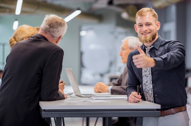 Retrato, de, sorrindo, homem negócios, mostrando, polegar cima, sinal, enquanto, equipe, discutir, em, a, fundo