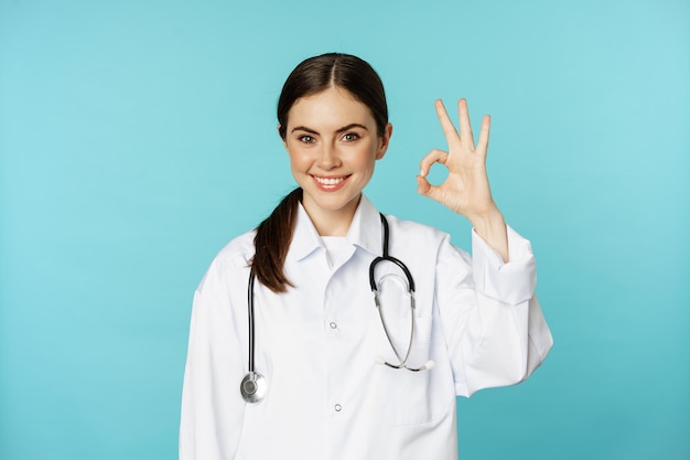 Retrato de trabalhador médico sorridente satisfeito, mulher, médico, mostrando tudo bem, zero, sem problema, gesto ex...