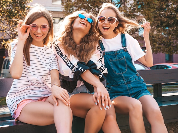 Retrato de três jovens bonitas garotas hipster sorridente em roupas da moda no verão. mulheres despreocupadas sexy, posando na rua. modelos positivos, se divertindo em óculos de sol.