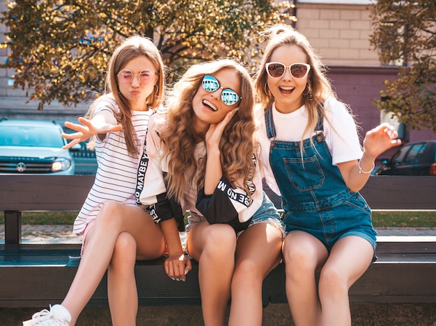 Retrato de três jovens bonitas garotas hipster sorridente em roupas da moda no verão. Mulheres despreocupadas sexy, posando na rua. Modelos positivos, se divertindo em óculos de sol.