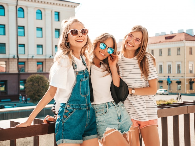 Retrato de três jovens bonitas garotas hipster sorridente em roupas da moda no verão. mulheres despreocupadas sexy, posando na rua. modelos positivos, se divertindo em óculos de sol.