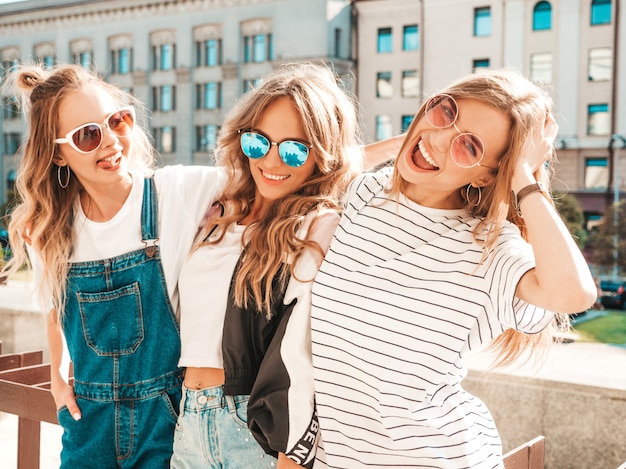 Retrato de três jovens bonitas garotas hipster sorridente em roupas da moda no verão. Mulheres despreocupadas sexy, posando na rua. Modelos positivos, se divertindo em óculos de sol.