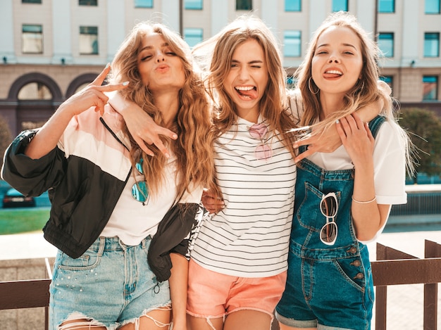Retrato de três jovens bonitas garotas hipster sorridente em roupas da moda no verão. Mulheres despreocupadas sexy, posando na rua. Modelos positivos se divertindo. Mostrando a língua