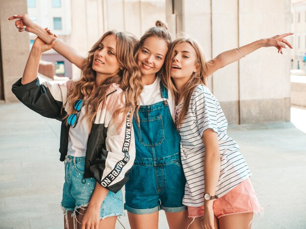 Retrato de três jovens bonitas garotas hipster sorridente em roupas da moda no verão. Mulheres despreocupadas sexy, posando na rua. Modelos positivos, se divertindo.