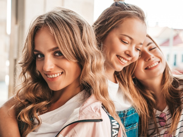 Retrato de três jovens bonitas garotas hipster sorridente em roupas da moda no verão. Mulheres despreocupadas sexy, posando na rua. Modelos positivos, se divertindo.