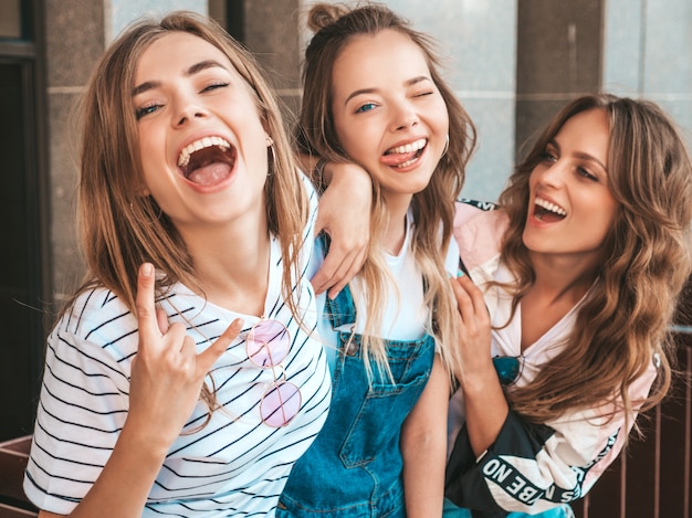 Retrato de três jovens bonitas garotas hipster sorridente em roupas da moda no verão. Mulheres despreocupadas sexy, posando na rua. Modelos positivos, se divertindo