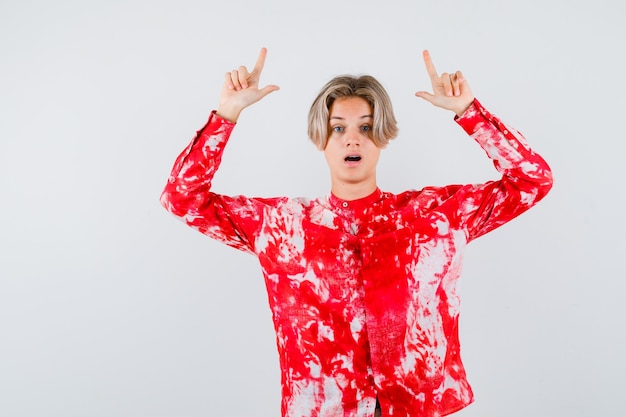 Retrato de um adolescente loiro apontando para cima com uma camisa grande e olhando confuso para a frente