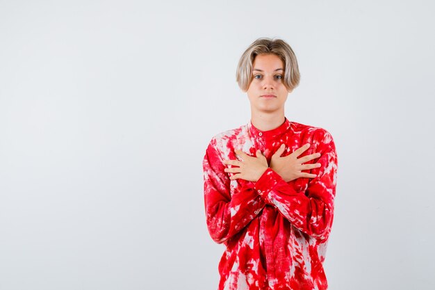 Retrato de um adolescente loiro segurando as mãos cruzadas no peito em uma camisa grande e olhando de frente com confiança