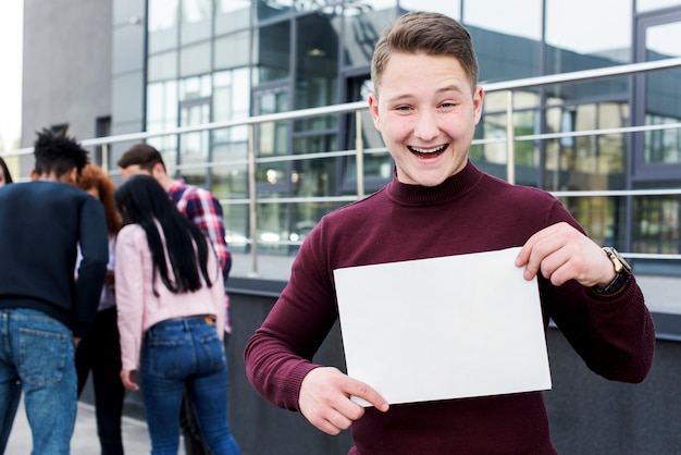 Retrato, de, um, alegre, homem jovem, segurando, vazio, painél publicitário, ficar, perto, predios