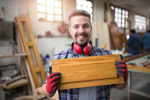 Retrato de um artesão sorridente segurando um móvel em sua oficina de carpintaria