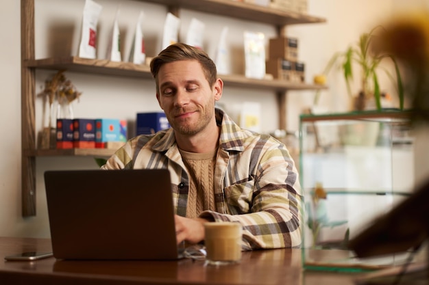 Retrato de um belo jovem nômade digital trabalhando em um café em um laptop parecendo feliz e satisfeito