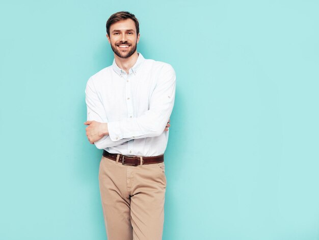 Retrato de um belo modelo sorridente Sexy homem elegante vestido de camisa e calças Moda hipster masculino posando perto da parede azul no estúdio isolado