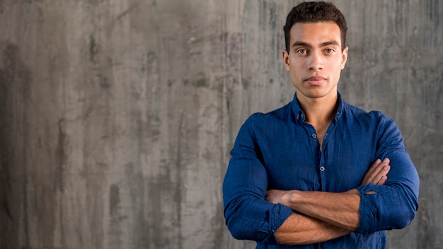 Foto grátis retrato, de, um, bonito, homem jovem, com, braços cruzados, contra, concreto, fundo