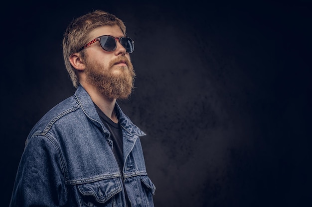 Retrato de um cara bonito hipster vestido com jaqueta jeans, olhando para longe. isolado em um fundo escuro.