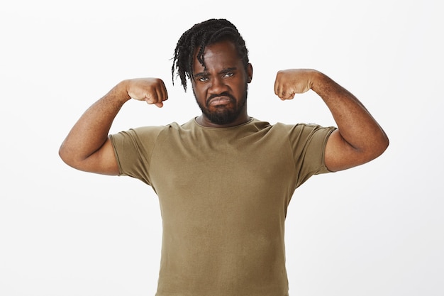Retrato de um cara sério em uma camiseta marrom posando contra a parede branca