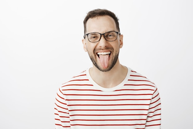 Retrato de um colega de trabalho adulto engraçado e bonito de óculos escuros, mostrando a língua e sorrindo alegremente, sendo despreocupado e descuidado com regras ou deveres