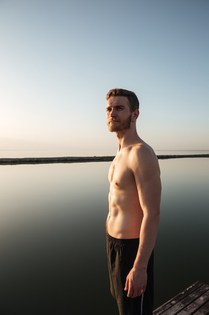 Retrato de um desportista sem camisa saudável em pé ao ar livre com água